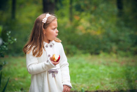 little girl is eating apple outdoorの写真素材