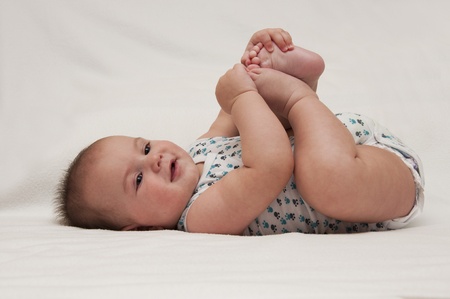 Baby boy lying and holding legsの写真素材