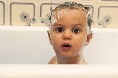 Cute little baby boy with big eyes it taking a foam bathの写真素材