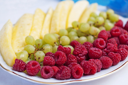 Healthy snack - pineapple, grapes and raspberries on a plateの写真素材