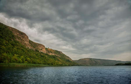 European river with hills. Forest on the beach. Storm clouds.