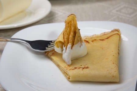 Piece of pancake in sour cream on a fork. Closeup.の写真素材