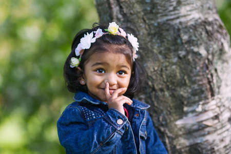 A funny small Asian girl at birch tree in city park