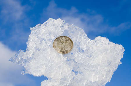 bit of ice wiht coin on blurred sky backgroundの写真素材