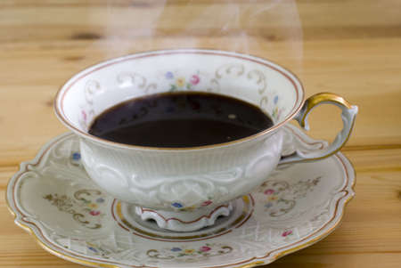 Antique cup with hot steaming coffee on the wooden surfaceの写真素材