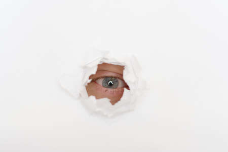 squinted eye of eavesdropper in the hole of white paperの写真素材