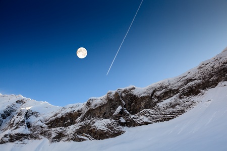 Full Moon and Airplane Trail in Blue Sky above Mountain Peak, French Alps, Megeveの写真素材