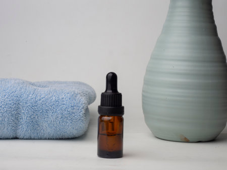 Essential oil in a glass bottle with a towel on a white background,a white skincare bottle with a plant flower theme on a white background and a blue towelの写真素材