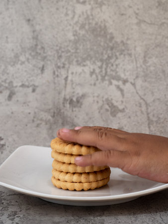 Hand holding a stack of cookies on a white plate with concrete backgroundの写真素材