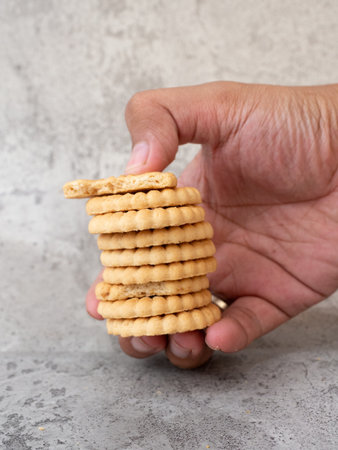 Hand holding a stack of crackers on a concrete background with copy space, biscuits stacked on a plate and some in hand, on a gray backgroundの写真素材