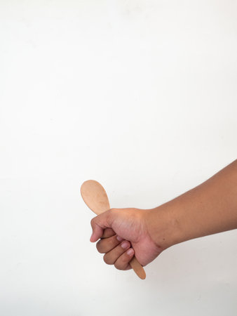 Hand holding a wooden spoon on white background with space for text.の写真素材