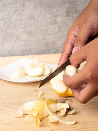 Man cutting pear on wooden cutting board with knife, selective focus.の写真素材
