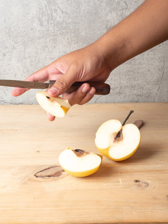 Cutting apple with knife on wooden board over concrete wall background.の写真素材