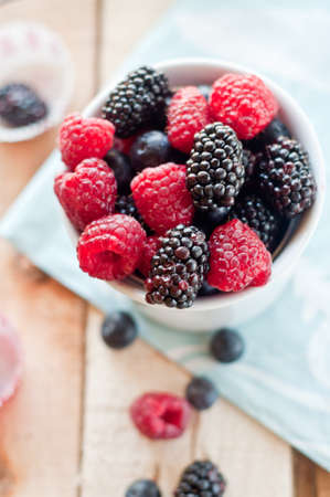 A bowl of fresh summer berries with blueberries, raspberries, blueberries set on a wooden background...