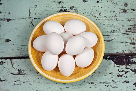 White eggs on a yellow plate, placed on a rustic wooden backgroundの写真素材