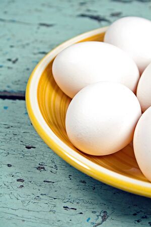 White eggs on a yellow plate, placed on a old shabby chic light blue wooden tableの写真素材