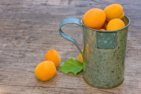 Apricots in an old rustic cup on a wooden backgroundの写真素材