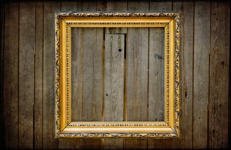 Golden empty frame on a wooden rustic wall with vintage textured editingの写真素材