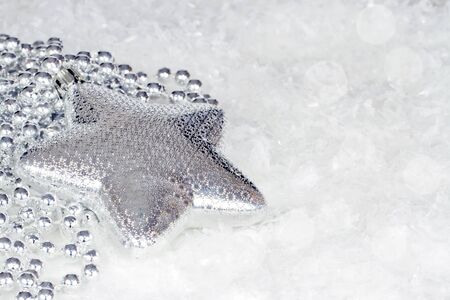 Silver Christmas star with silver decorative beads with snowflakes and bokeh backgroundの写真素材