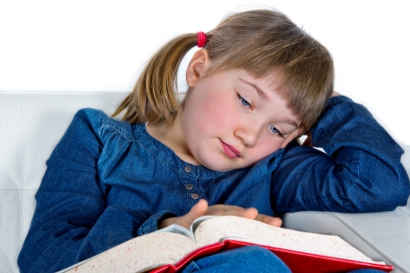 Cute girl reading a book sitting on a white couchの写真素材