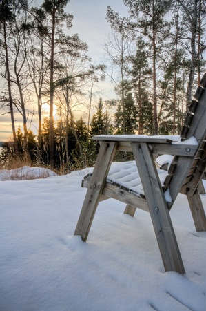 Empty chair covered with snow, facing and evening sunset and snowy wintry landscapeの写真素材
