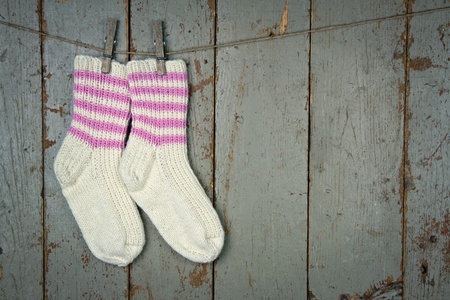 Two white woolen socks with pink stripes hanging from clothespins in front of wooden rustic backgroundの写真素材