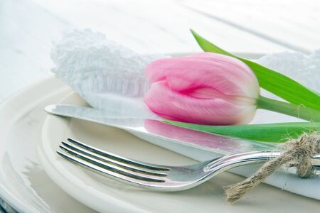 Closeup of pink tulip at rustic dinner setting, on white wooden tableの写真素材
