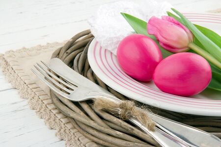 Easter dinner setting with two pink eggs and tulip, rustic white wooden backgroundの写真素材