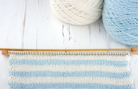 Knitting on white wooden background, light blue and white stripesの写真素材