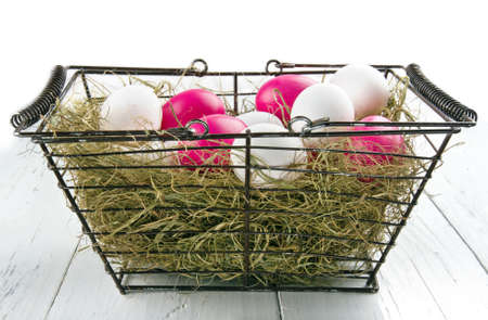 Shopping basket with easter eggs and dried hay on wooden white backgroundの写真素材