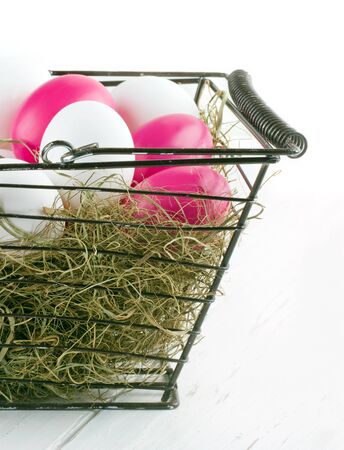 Shopping basket with easter eggs and dried hay on wooden white backgroundの写真素材