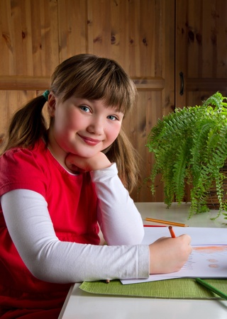 Cute little girl smiling and drawing with color pencils at her deskの写真素材