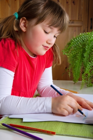 Cute little girl drawing with color pencils at her deskの写真素材