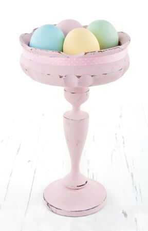 Vintage pastel color easter eggs in old elegant vase on white wooden backgroundの写真素材