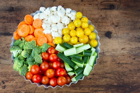 Arrangement of vegetables in a round metal tray as slices, on rustic wooden backgroundの写真素材