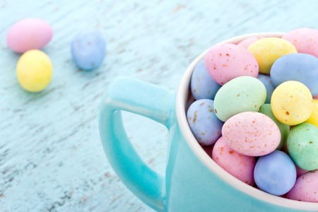 Small pastel easter eggs in a light blue cup on vintage wooden background
