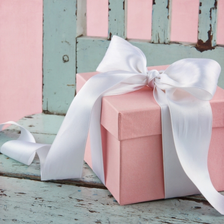 Pink romantic gift box with white satin bow on a light blue wooden chairの写真素材