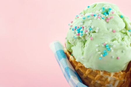 Green pear ice cream in a cone on pink background with copy space