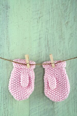 Pink baby girl mittens on clothesline on green vintage wooden backgroundの写真素材