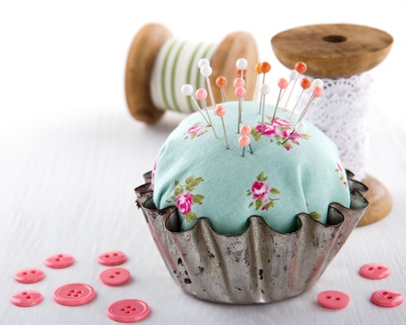 Green handmade floral pincushion in an old metal cupcake with buttons and spools of thread and lace, sewing concept backgroundの写真素材