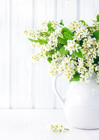 Bouquet of white bird cherry branches in a ceramic jug on vintage wooden tableの写真素材