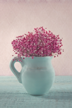 Pink dried baby's breath flowers in a blue jug on wooden background and vintage wallpaperの写真素材