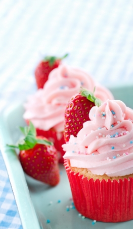 Pink cupcakes with fresh strawberries and sprinkles on a vintage tray and blue retro towelの写真素材