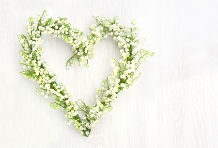 Heart shaped flower wreath of lilys of valley on white wooden background