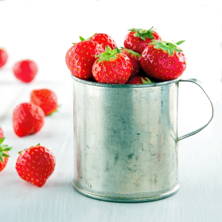 Fresh red strawberries in an old metal measurement cup on vintage white wooden backgroundの写真素材