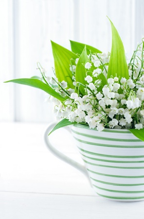Bouquet of lily of the valley spring flowers in a green striped cup on white vintage backgroundの写真素材