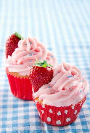Pink cupcakes with fresh strawberries and sprinkles on a vintage blue retro towel and copy spaceの写真素材