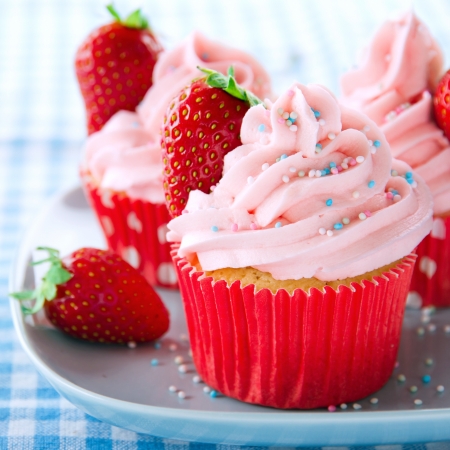 Pink cupcakes with fresh strawberries and sprinkles on a vintage tray and blue retro towelの写真素材