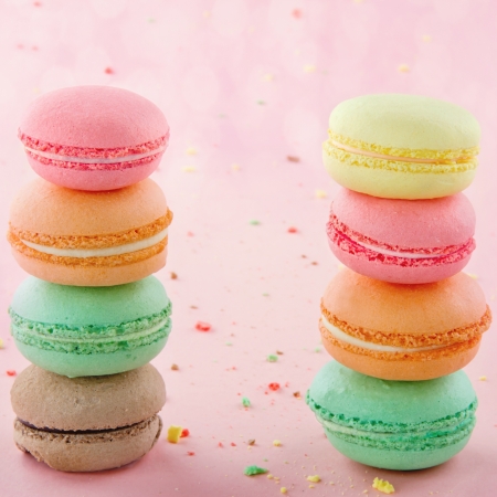 Two piles of colorful macaroons on pastel pink background with small crumbsの写真素材