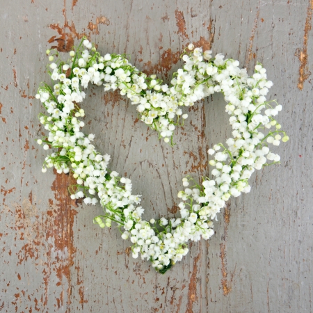 Heart shaped flower wreath of lilys of the valley on green wooden backgroundの写真素材